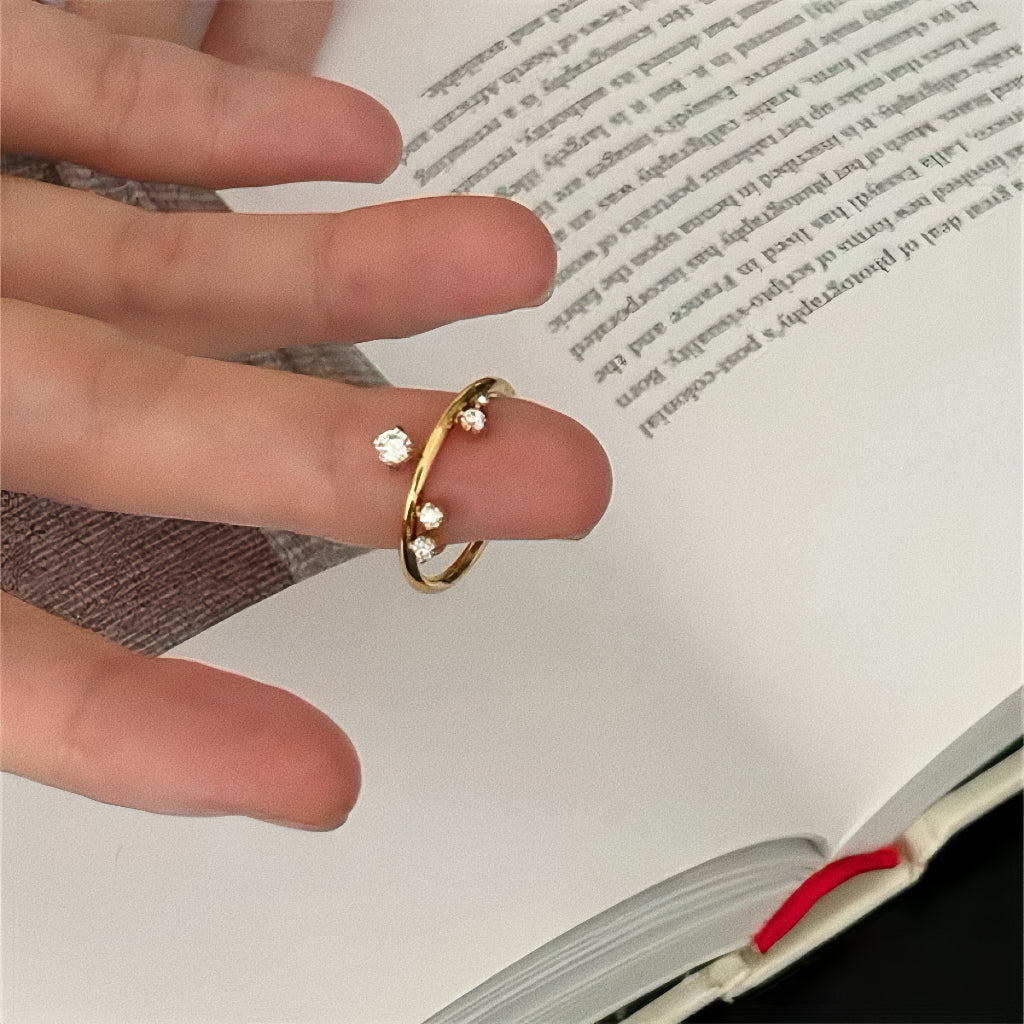 Woman wearing the Stella Constellation Ring on index finger, showing the scattered crystal design against a book page.