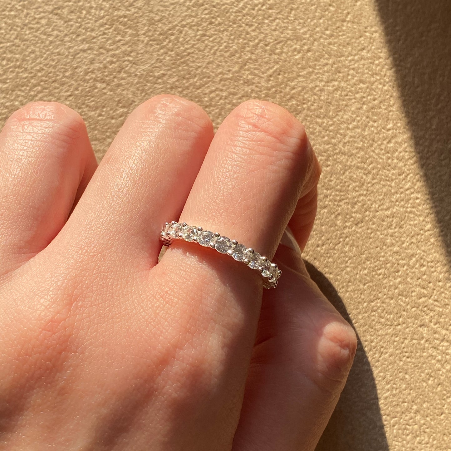 Sterling silver dainty ring catching sunlight on hand.