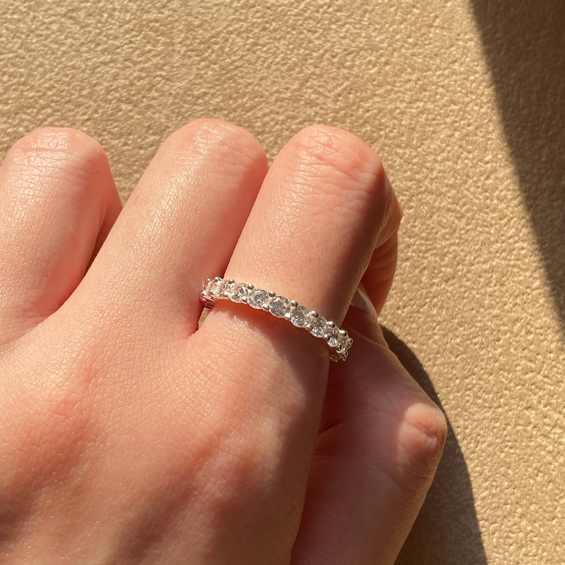 Sterling silver dainty ring catching sunlight on hand.