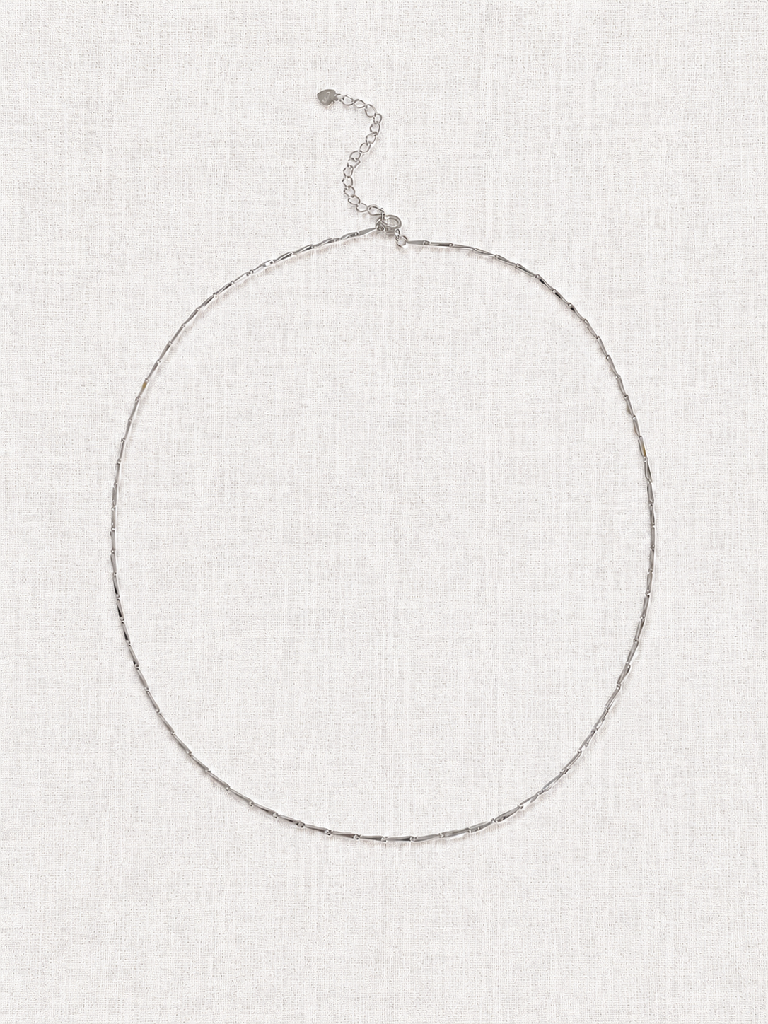 Full length flat lay of a dainty sterling silver bar chain necklace with extender, a fine layering chain on linen