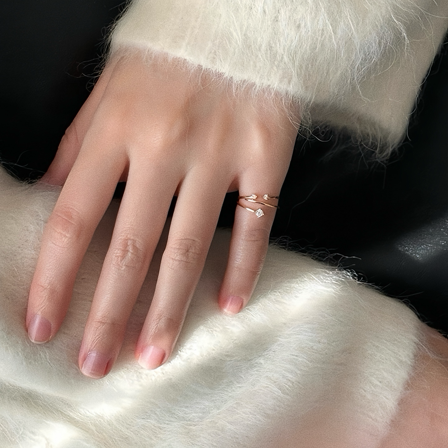 Minimal gold stacking rings including dainty open pinky ring with single cubic zirconia on hand in soft white knit jumper