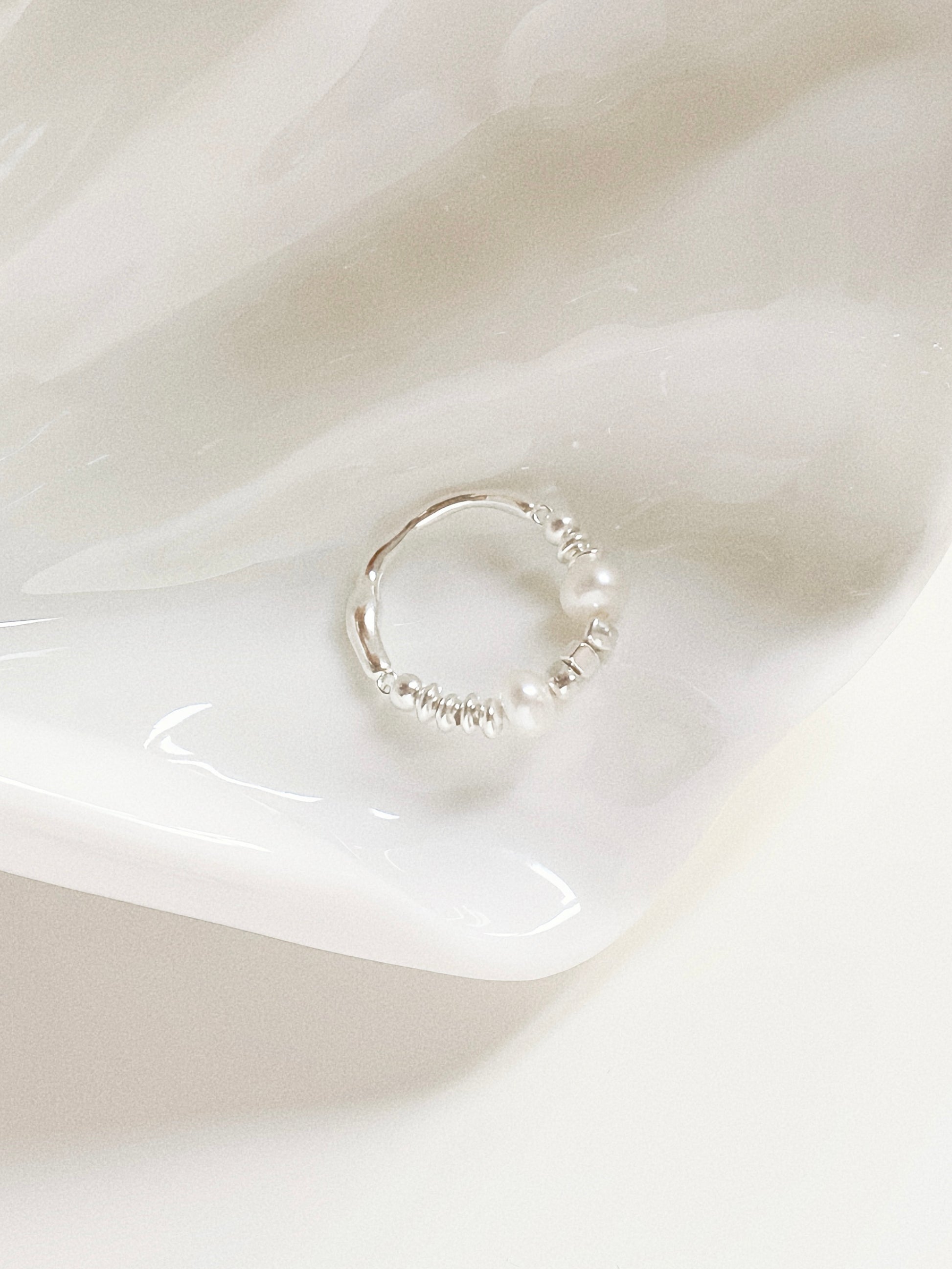 The stretchy freshwater pearl ring resting elegantly inside a white decorative shell-shaped tray.