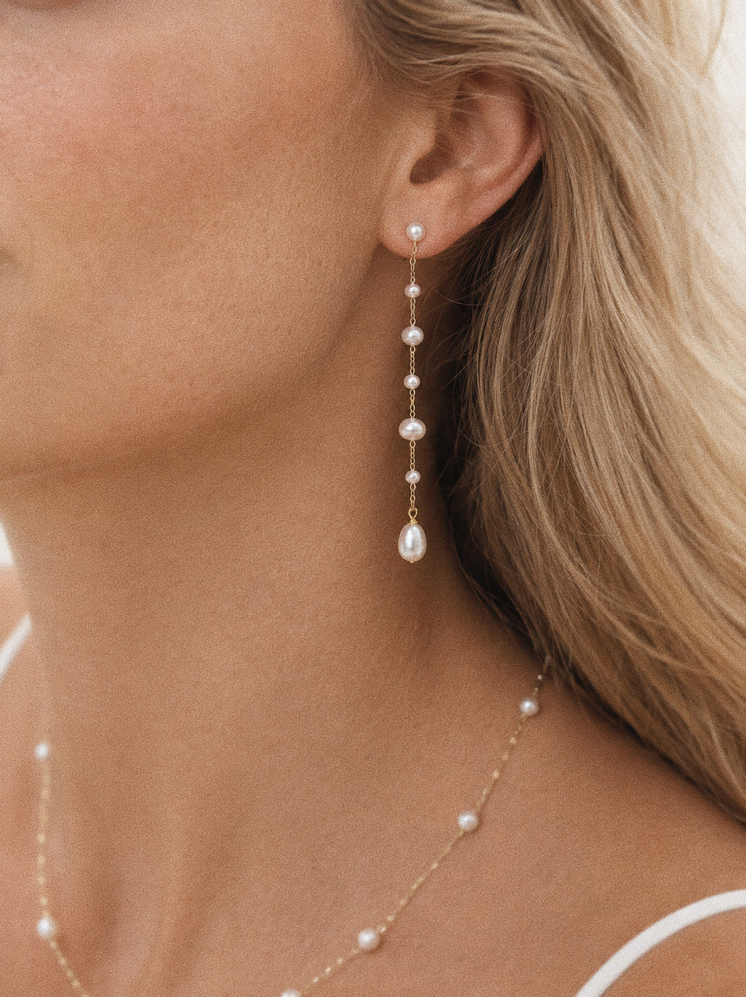 Sway long pearl dangle earrings worn on the ear, showing the fine gold chain, spaced cultured pearls and teardrop finish.