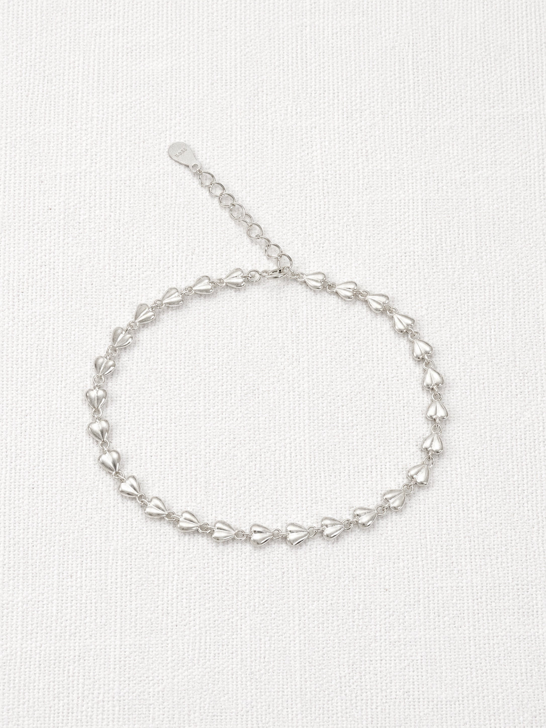 Dainty 925 sterling silver bracelet made of tiny linked puffed love hearts with an extender chain on a white linen background