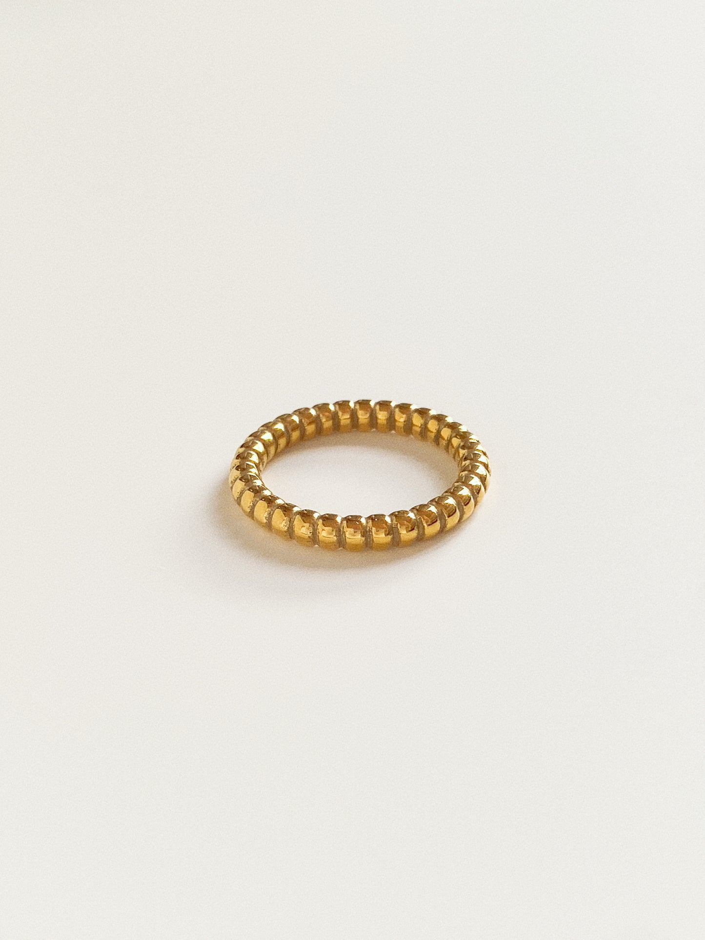 Close-up of a wide gold beaded band ring showing the high-polished titanium texture.