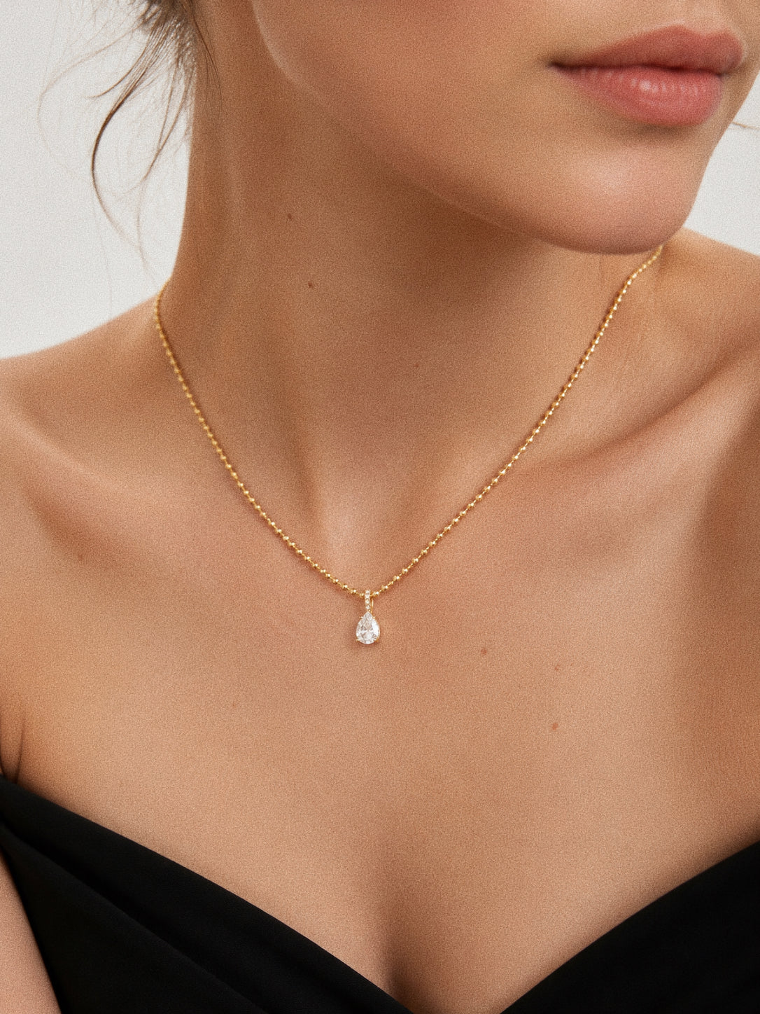 Model wearing the Dew teardrop necklace with the pear pendant sitting at the collarbone in 18k gold