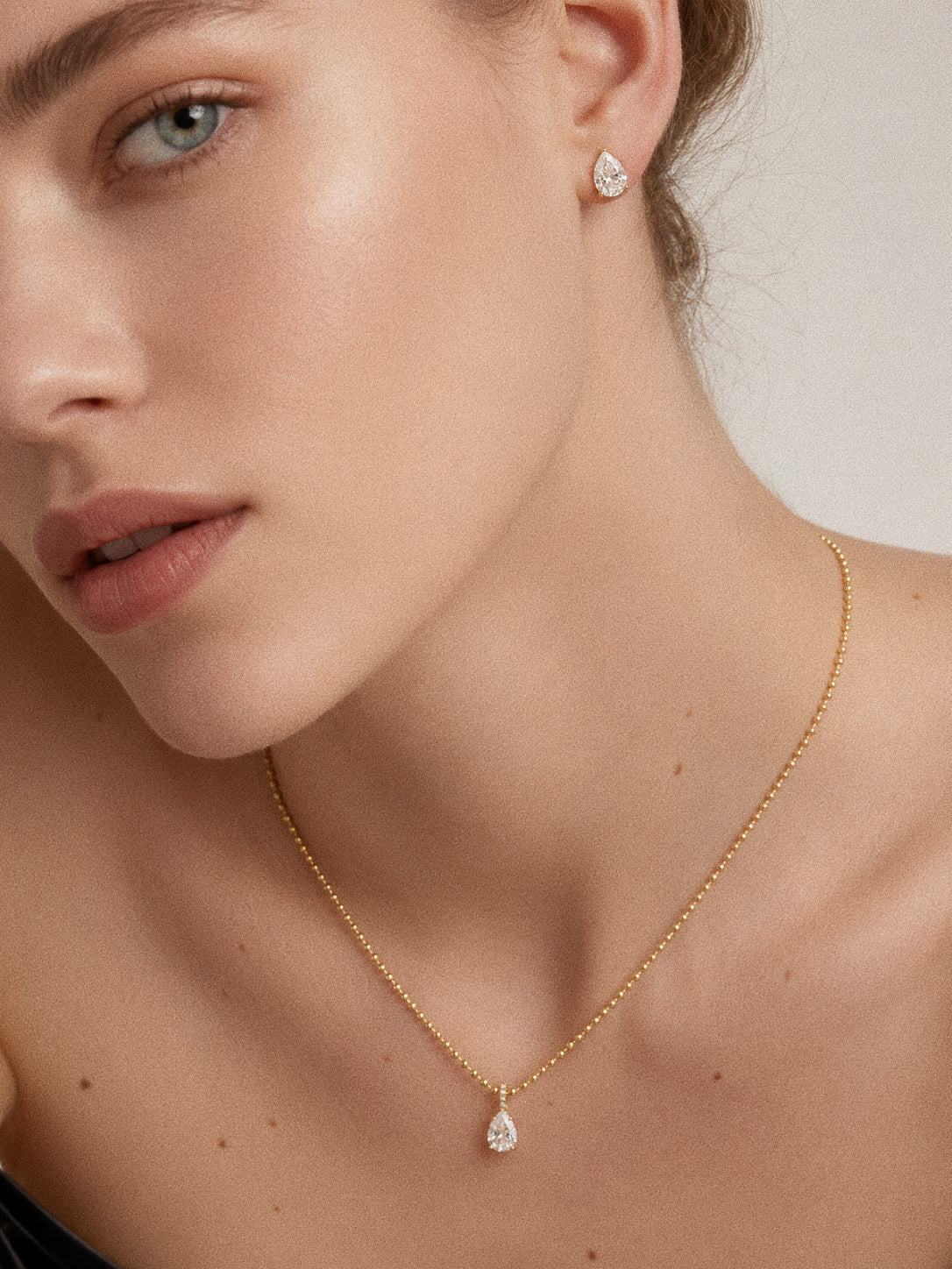 Model wearing the Dew teardrop set with pear studs and matching pendant necklace in 18k gold
