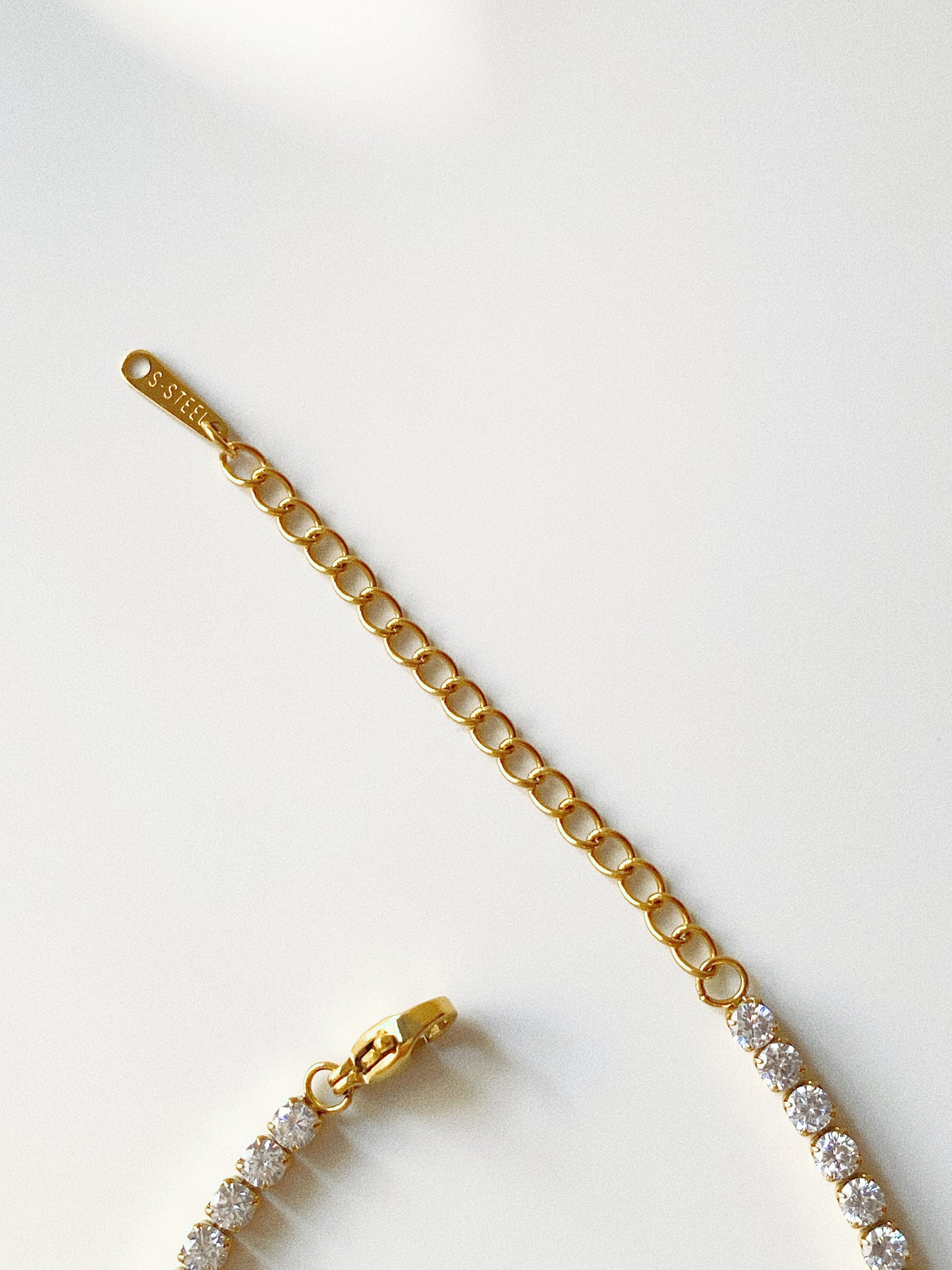 Gold tennis bracelet showing stainless steel extension chain and stamped quality tag detail