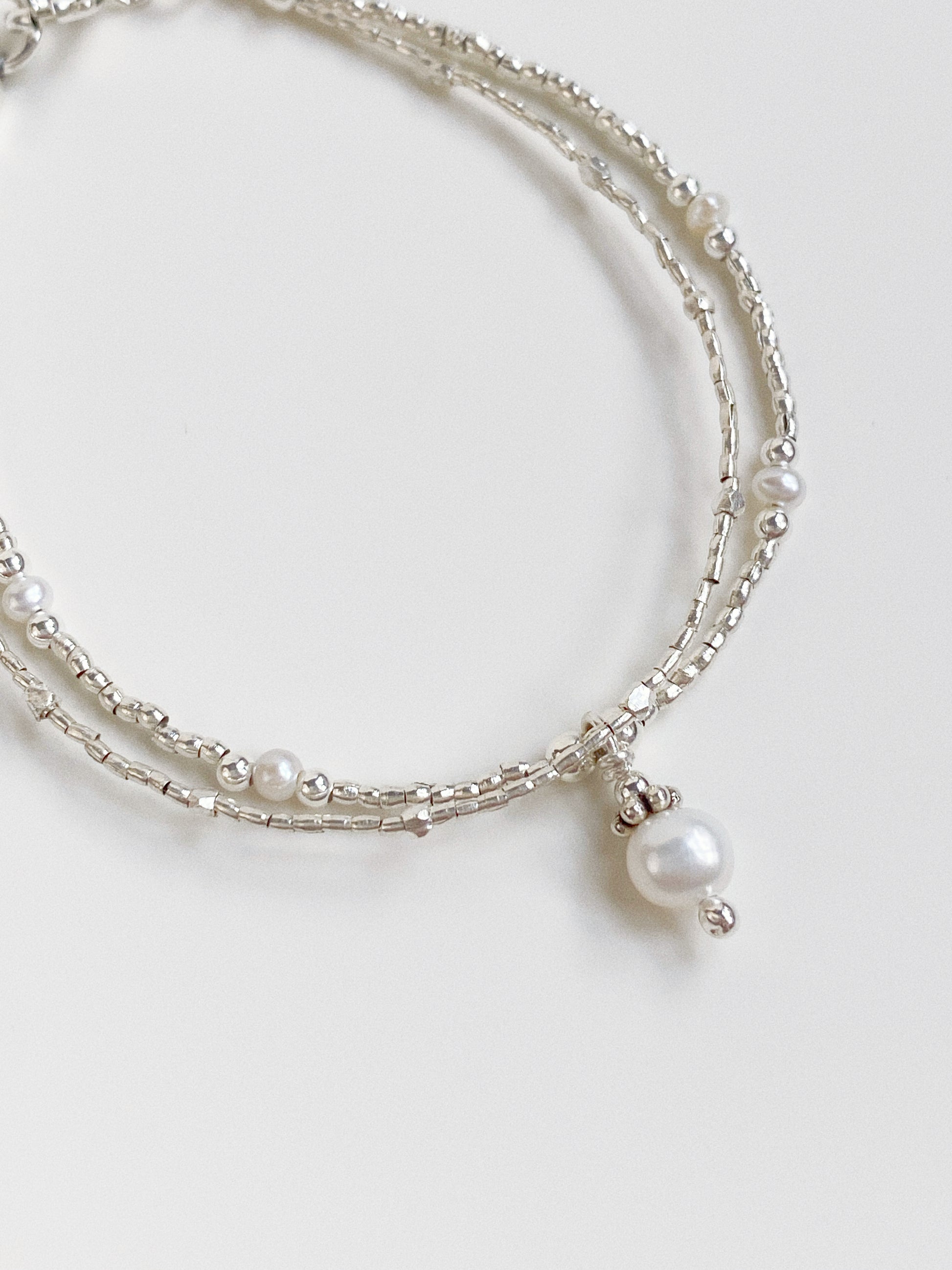 Close-up of textured Thai silver beads and high-lustre pearls on a structured professional steel wire.