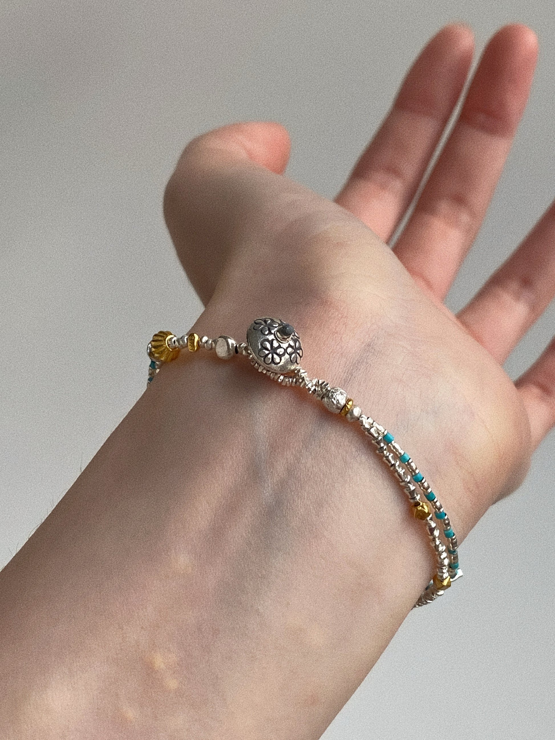 Hand-stamped Thai silver flower bead clasp on natural turquoise double-layer bracelet worn on wrist