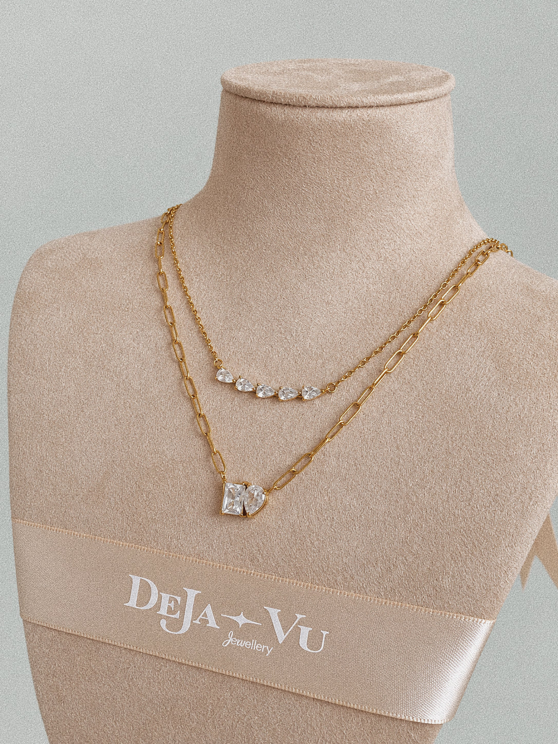 Toi et Moi gold paperclip necklace layered below a five-stone necklace on an angled beige jewellery bust.