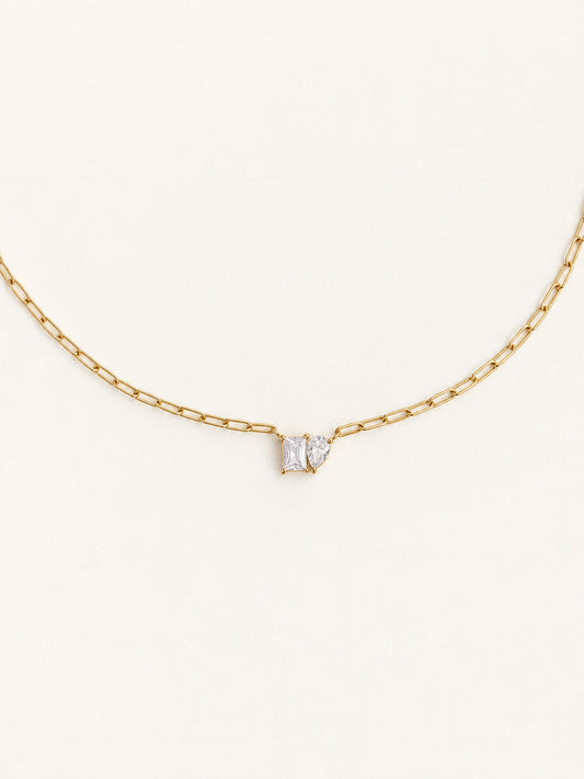 Toi et Moi necklace with rectangular and pear-shaped clear stones on a gold paperclip chain against an ivory background.