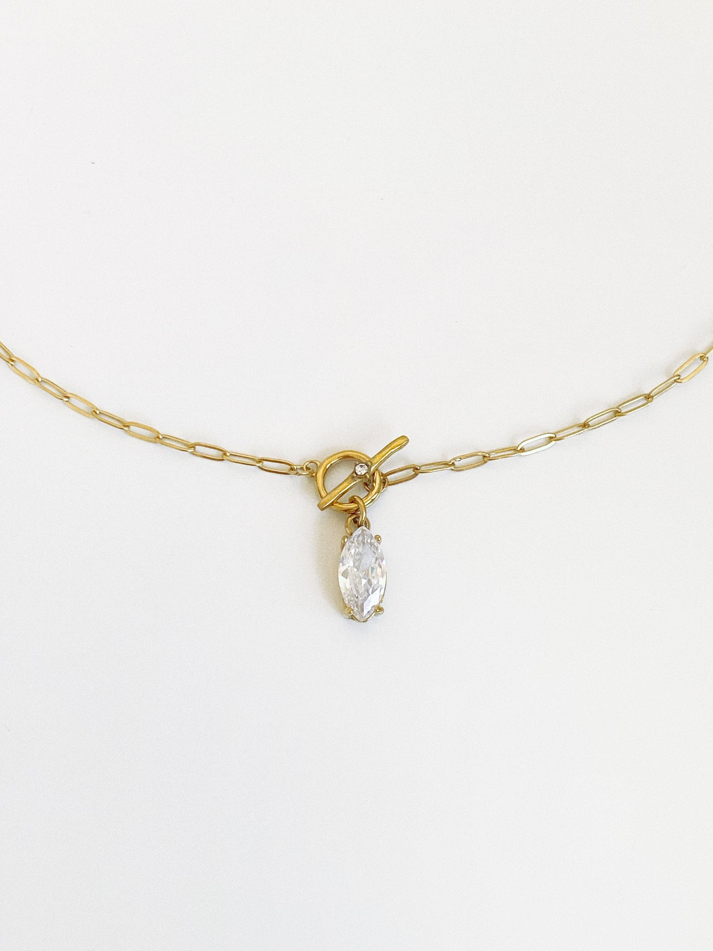 Close-up of the front toggle clasp and dangling marquise zircon drop on a fine gold paperclip chain