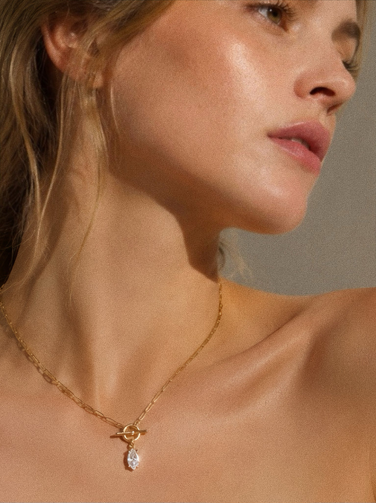 Side profile of a model in warm sunlight wearing the gold marquise drop toggle necklace against bare collarbone