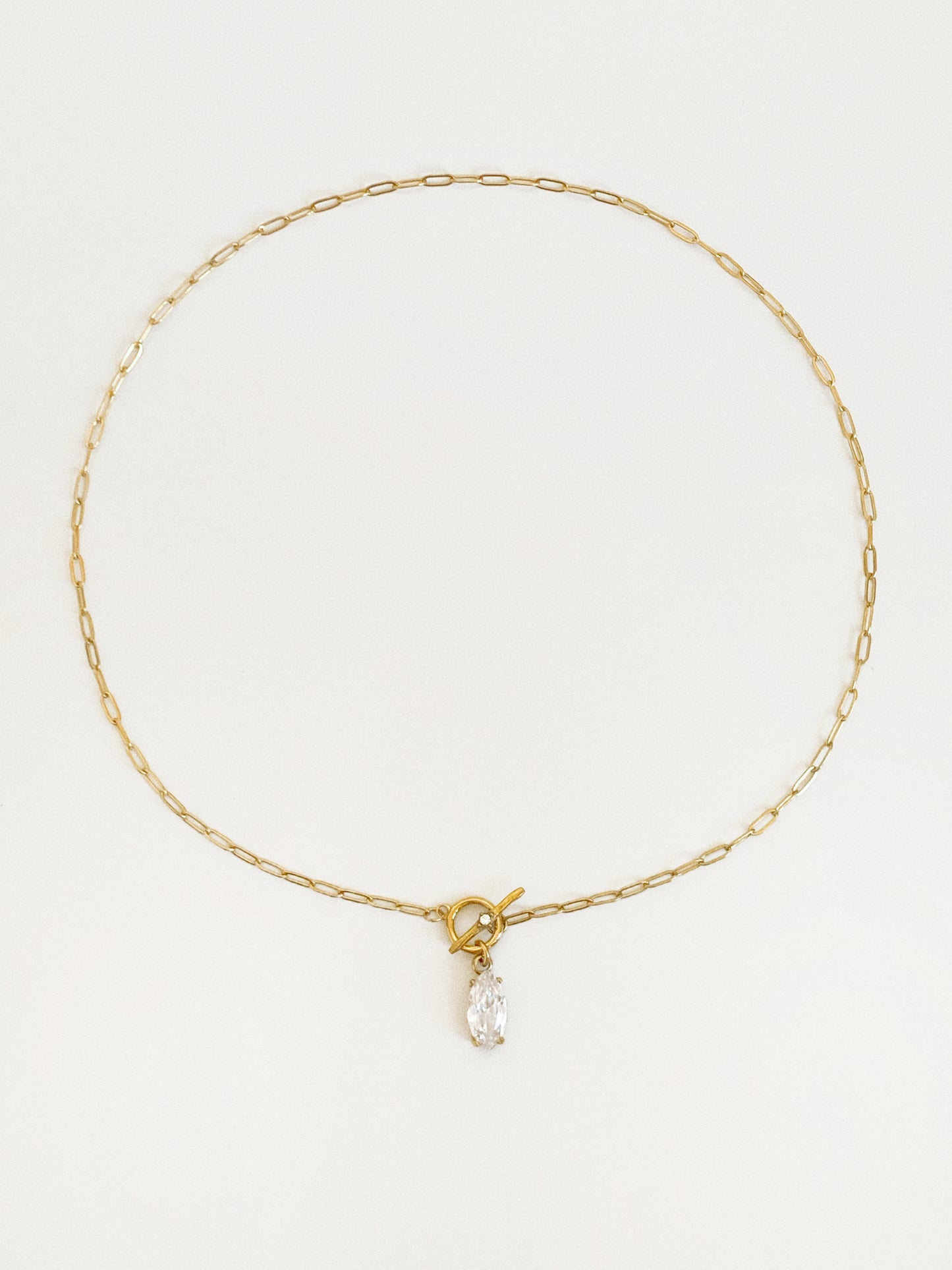 Gold paperclip chain necklace laid in a circle with a front T-bar toggle clasp and a marquise-cut cubic zirconia drop at the centre