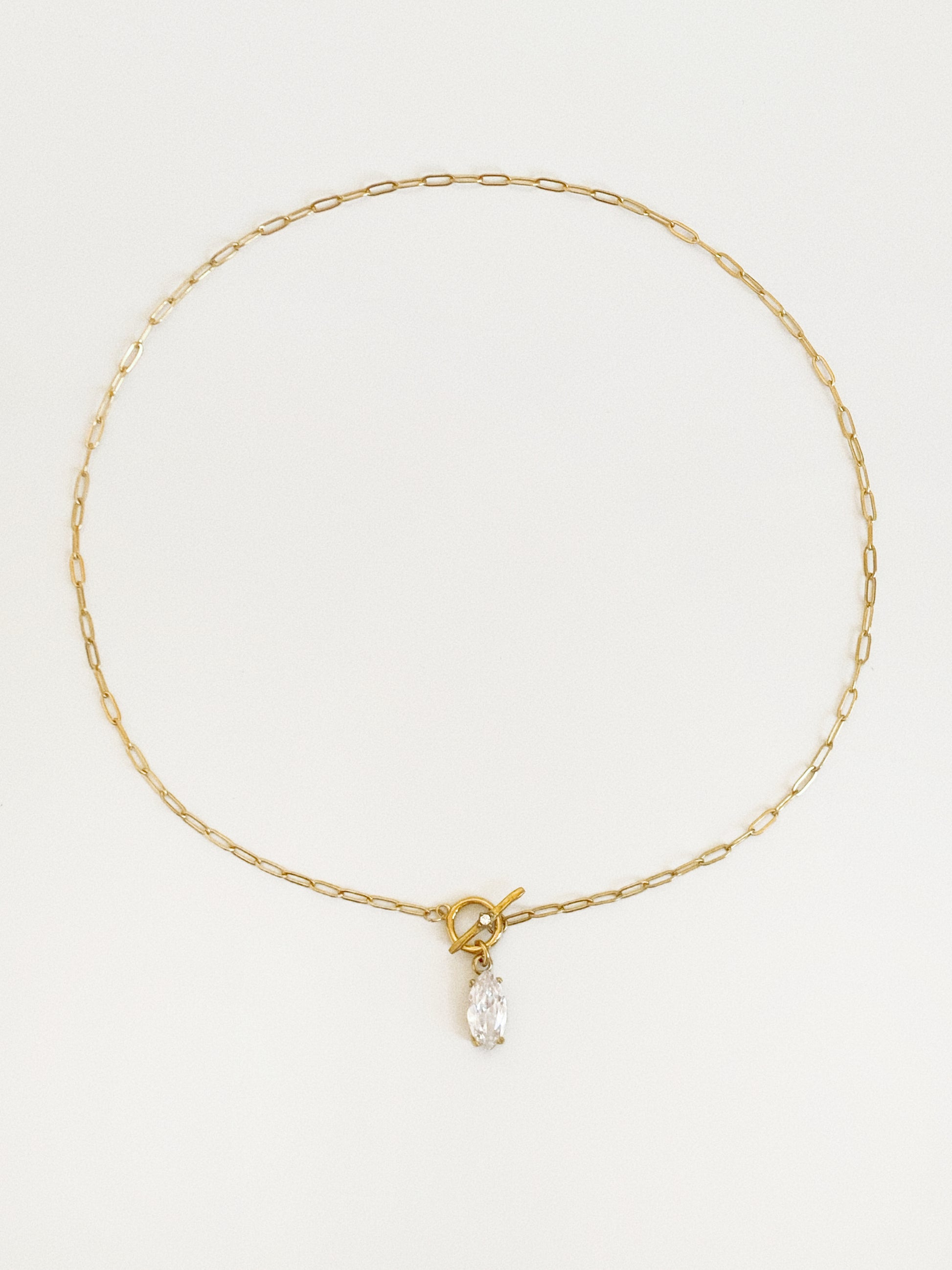 Gold paperclip chain necklace laid in a circle with a front T-bar toggle clasp and a marquise-cut cubic zirconia drop at the centre
