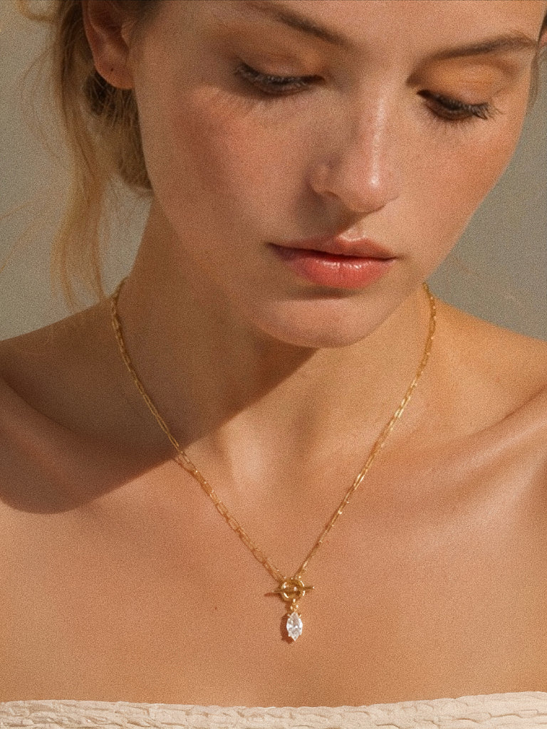 Model wearing the gold paperclip chain necklace with the front toggle clasp and marquise drop sitting just below the collarbone in soft light