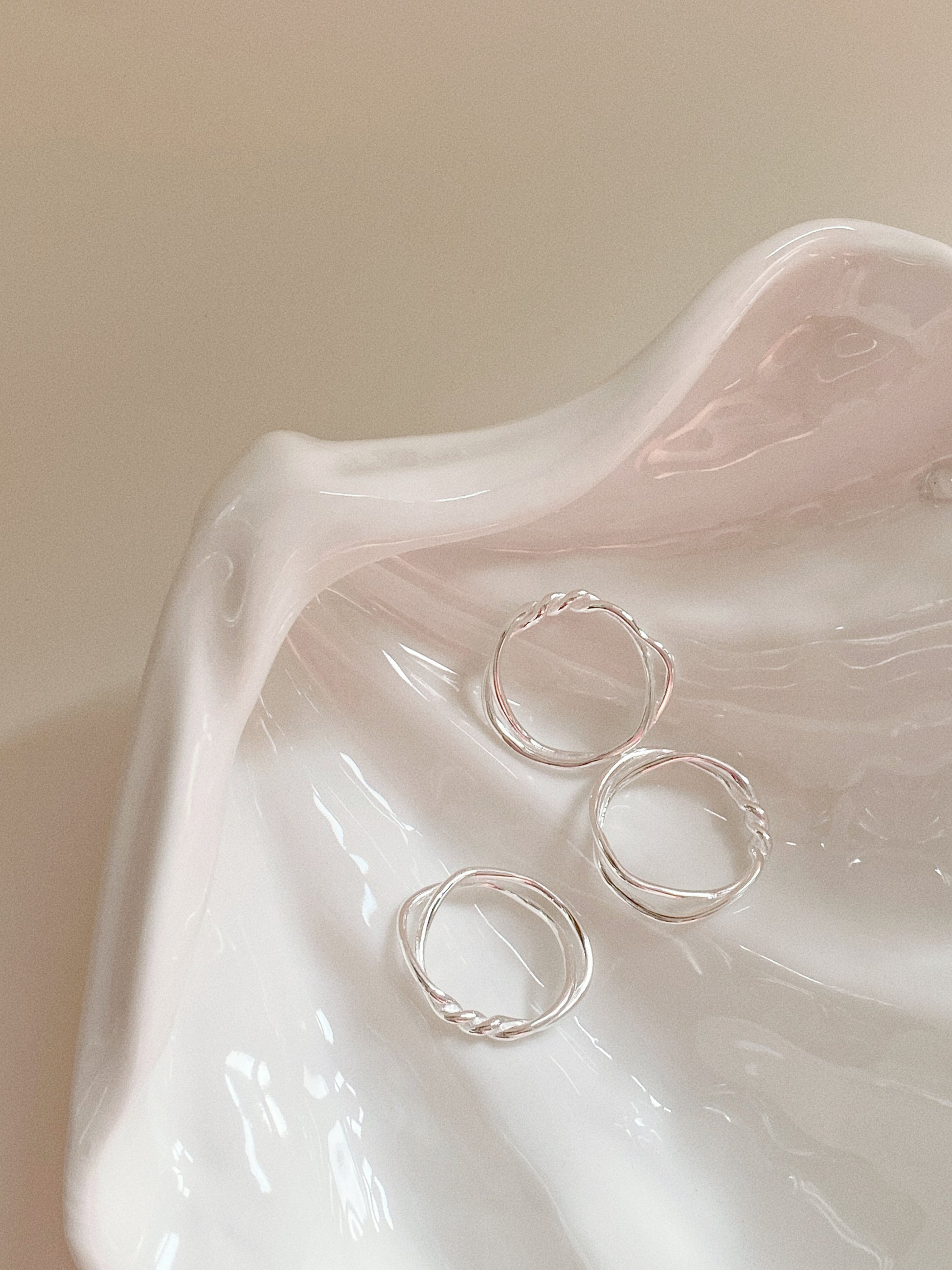 Three Twin Tide twisted silver rings displayed inside a white porcelain shell tray.