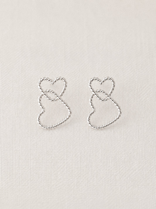 Sterling silver twisted wire double heart stud earrings with two interlocking rope-textured hearts on a soft linen background
