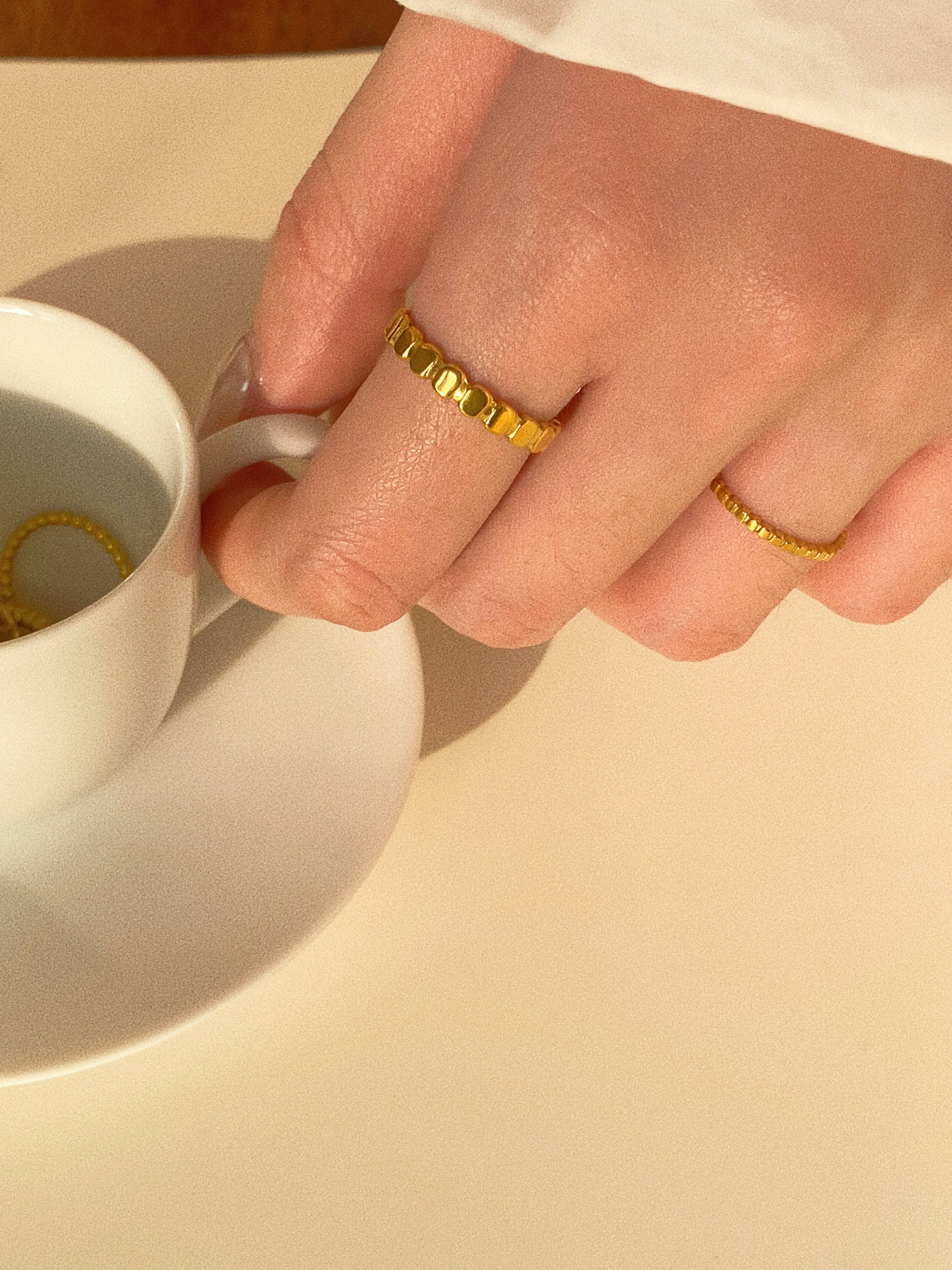 A woman wearing the wide beaded oval ring while holding a coffee cup, showcasing its everyday fashion appeal.