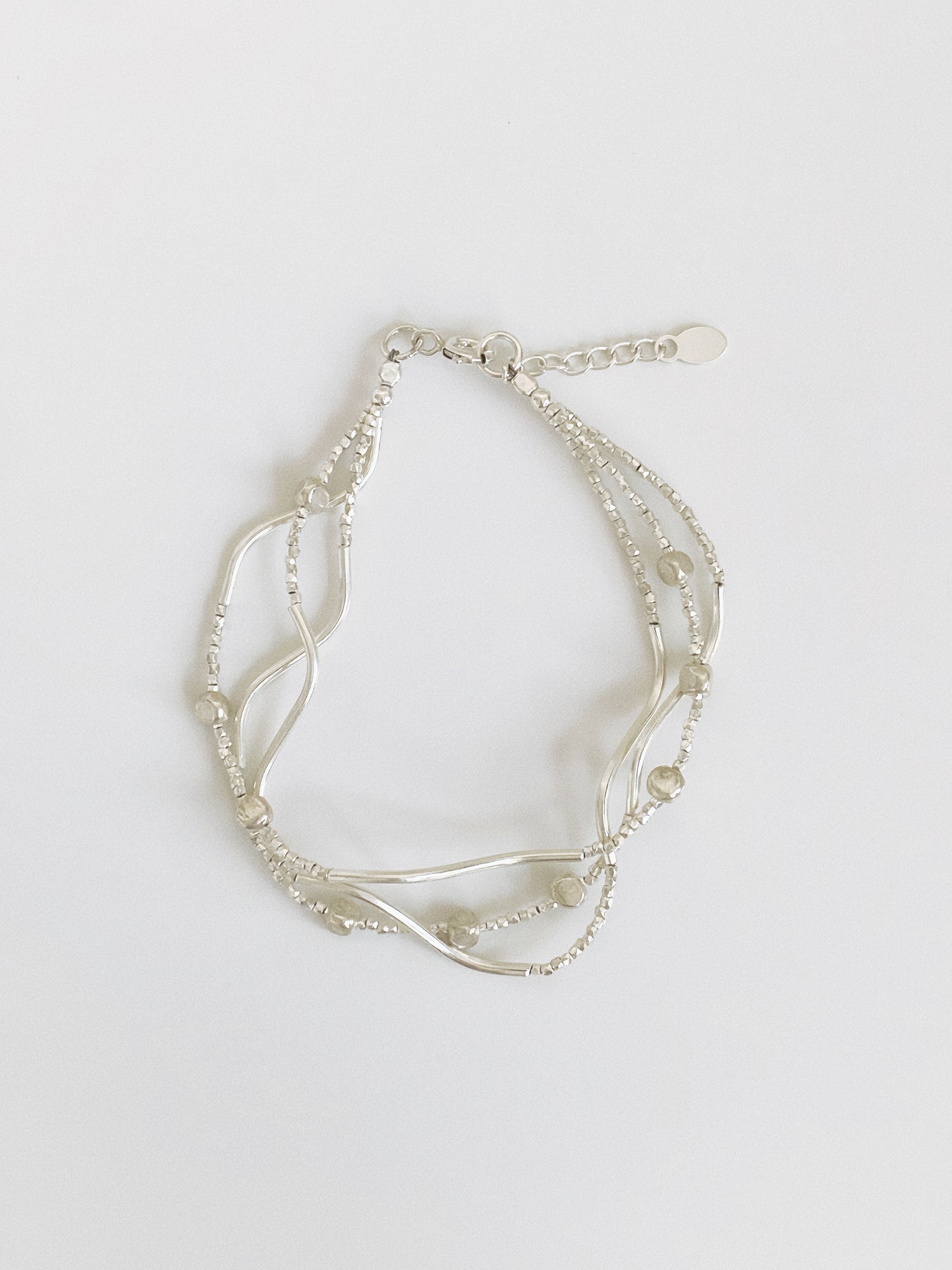 Multi-strand sterling silver bracelet with wavy curved bars, tiny faceted silver beads and pebble accents, shown flat with extender chain