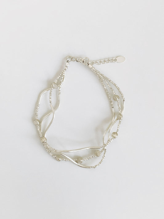 Multi-strand sterling silver bracelet with wavy curved bars, tiny faceted silver beads and pebble accents, shown flat with extender chain