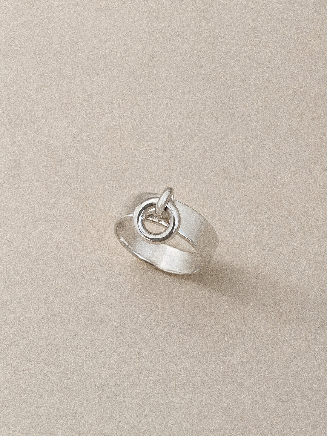 Close view of the silver charm ring showing its solid dangling hoop resting on the wide polished band.
