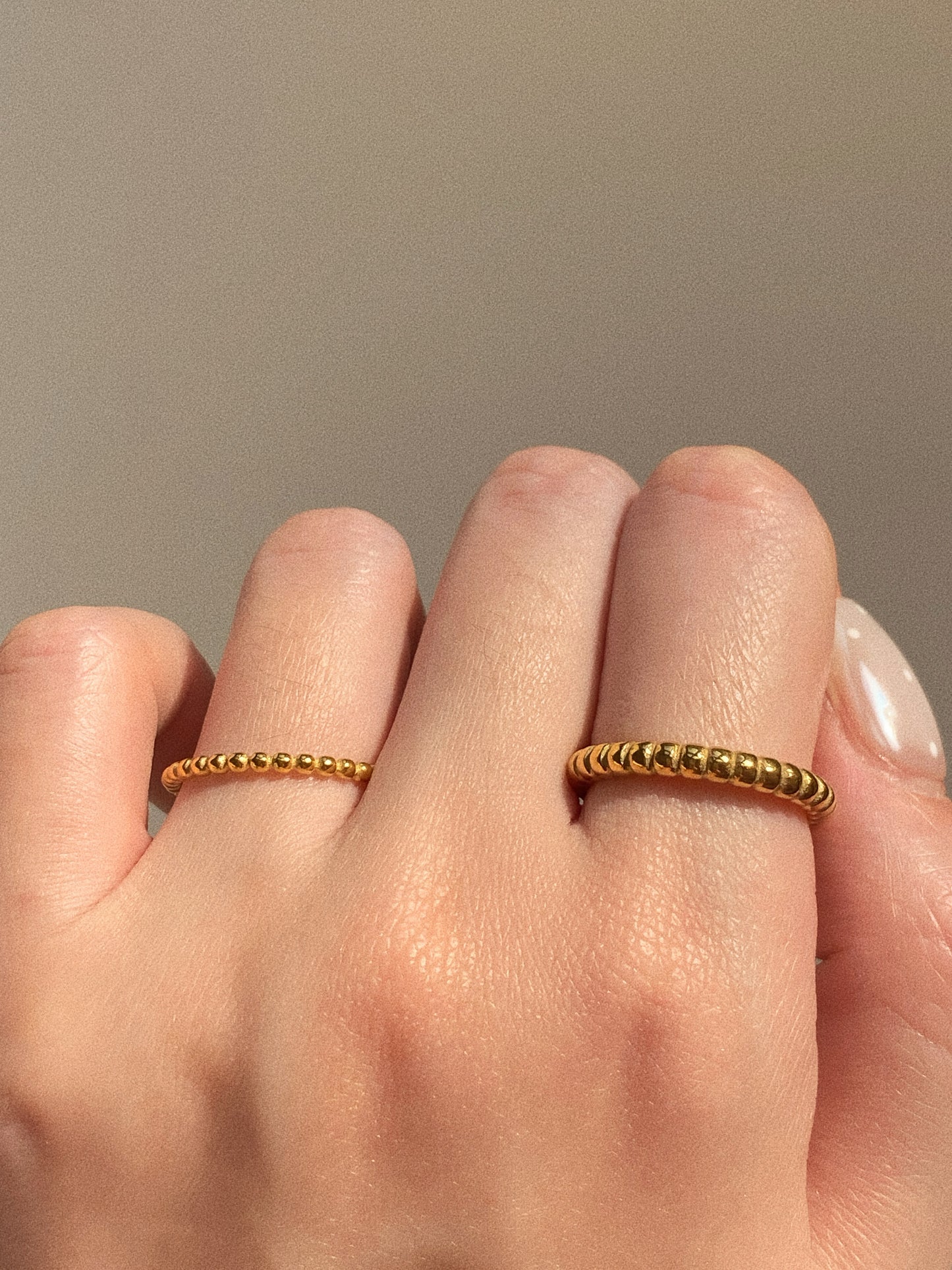 A woman's hand wearing the wide and narrow gold beaded rings, showing a modern stack.