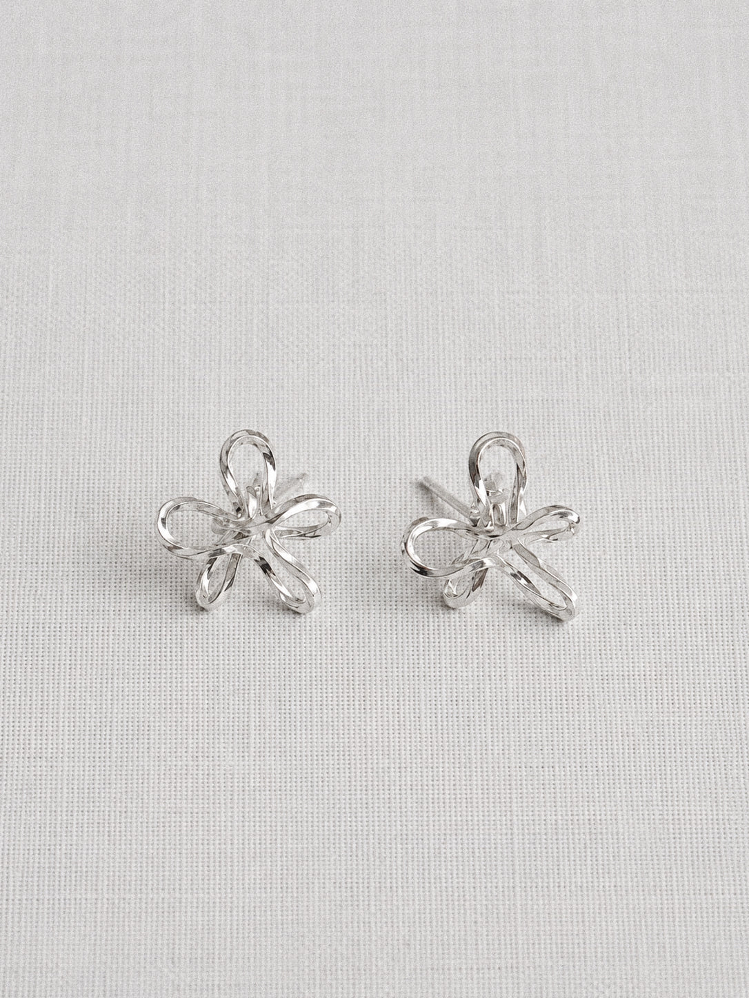 Handmade sterling silver wire flower stud earrings with looped petal design on a linen background by Deja Vu